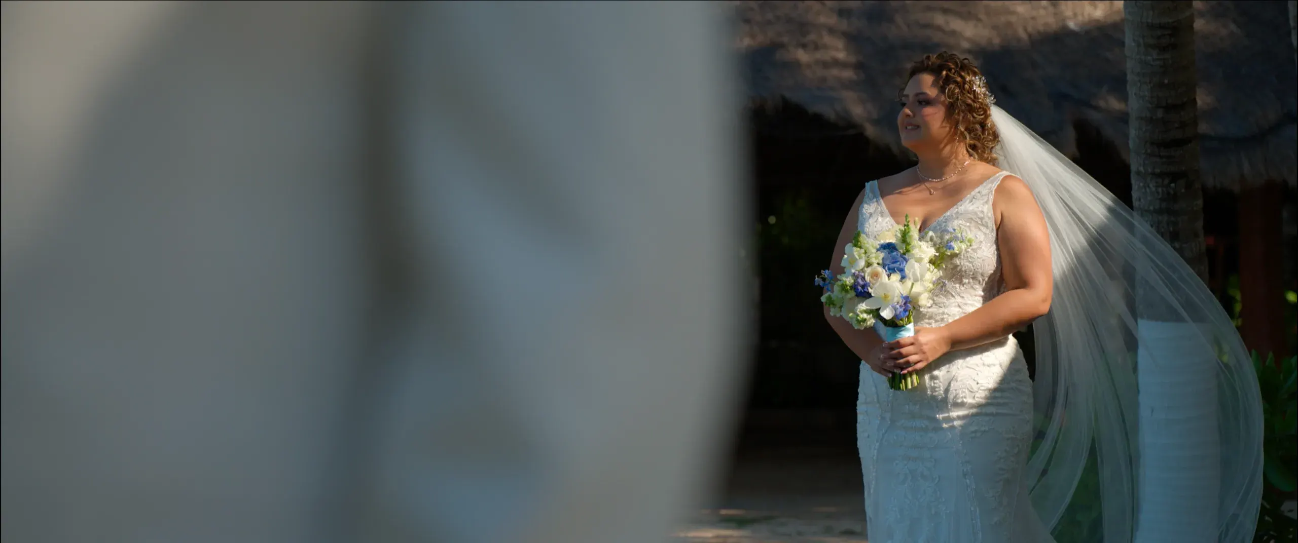 Fiorela holding her bouquet beside a palapa at Ocean Events, an independent venue in Costa Mujeres.