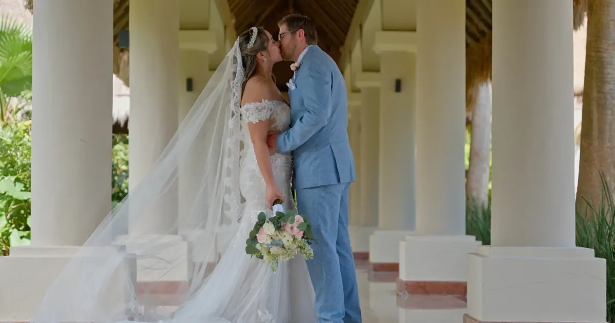Novia y novio besándose bajo una columnata junto a un estanque de lirios.