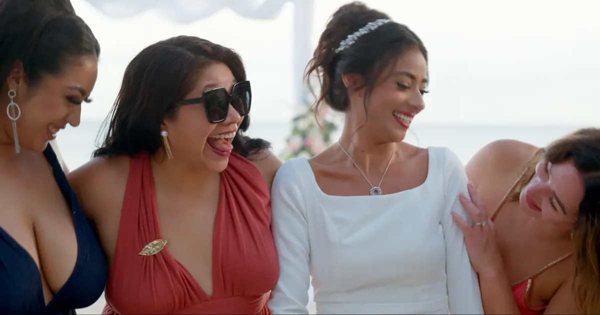 Novia riendo con sus damas en una boda frente al mar.