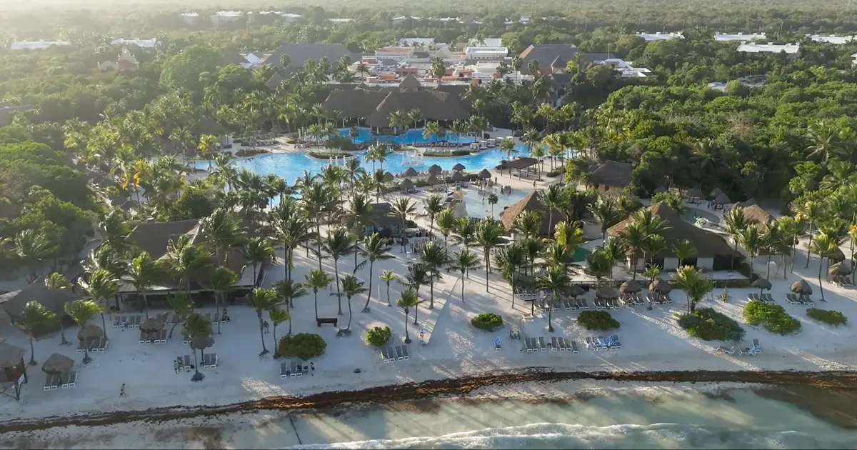 Vista aérea de un resort todo incluido de playa con albercas, palapas y palmeras en la costa de la Riviera Maya.