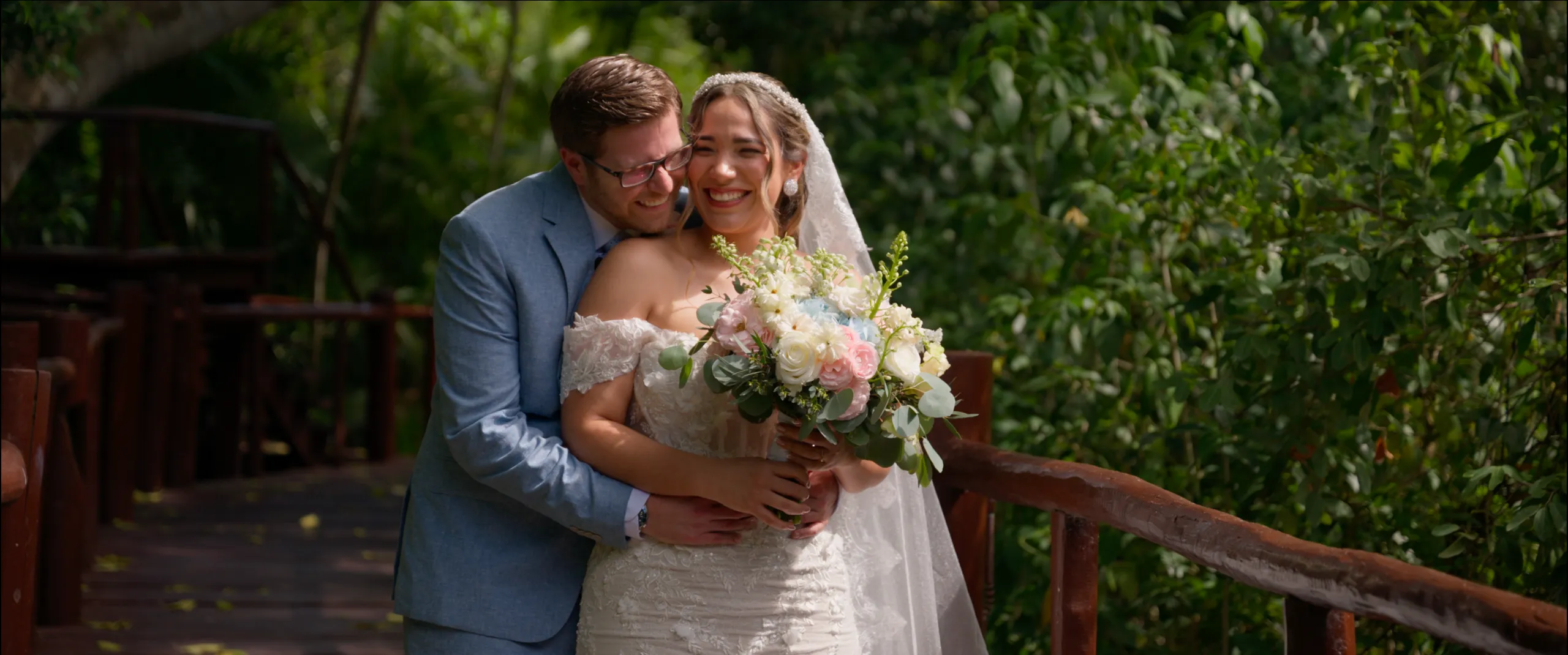 Diana y Zach abrazados en un puente de madera rodeado de vegetación de selva en el Grand Palladium Colonial Resort.