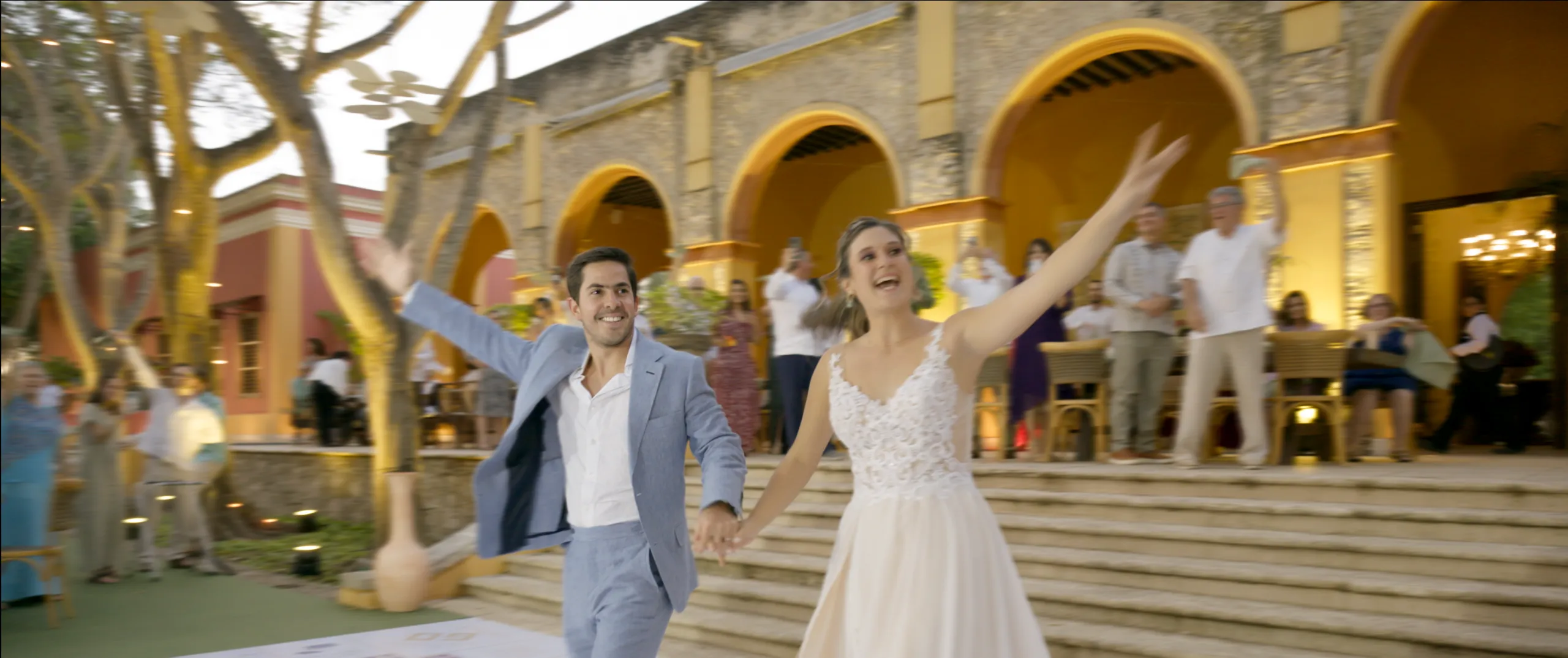 María and Fernando making their reception entrance under the arches of Hacienda Xtepen as guests cheer.