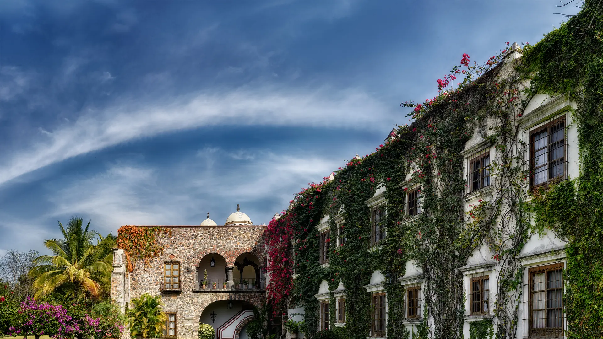 The ivy-covered colonial facade of Hacienda de Acamilpa in Morelos, with bougainvillea over the stone arcade.