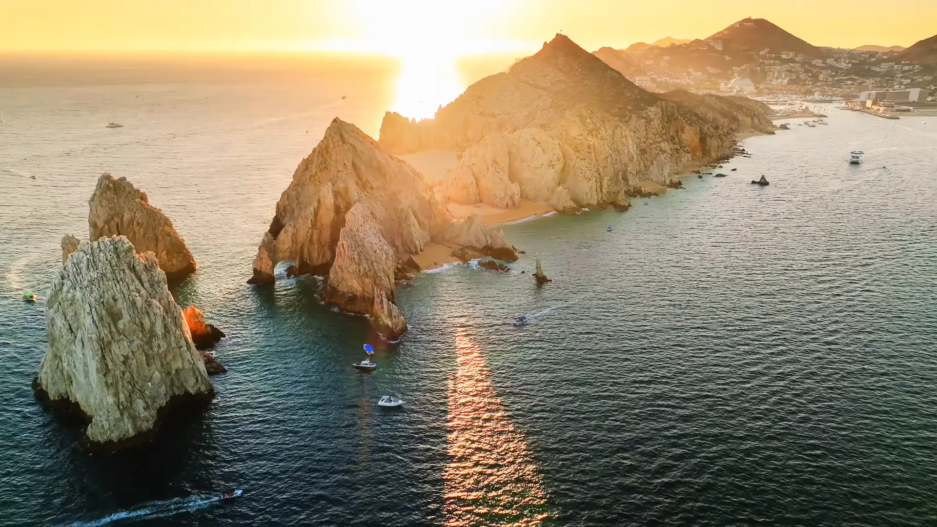 El sol metiéndose sobre el mar en Land's End, Cabo San Lucas, con El Arco y la Marina al fondo.