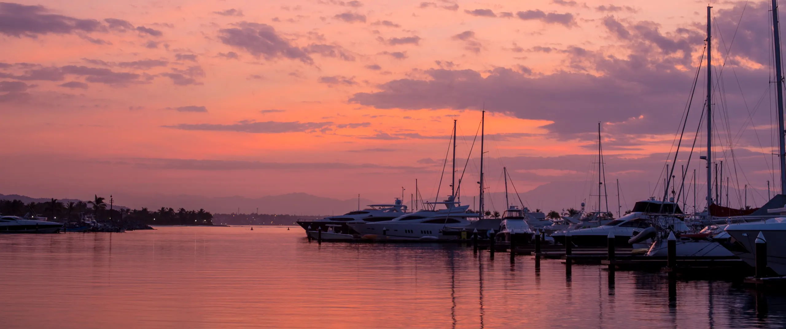 Primera luz sobre la marina de Nuevo Vallarta, en la Bahía de Banderas, con yates y veleros amarrados y las montañas detrás de la bahía.