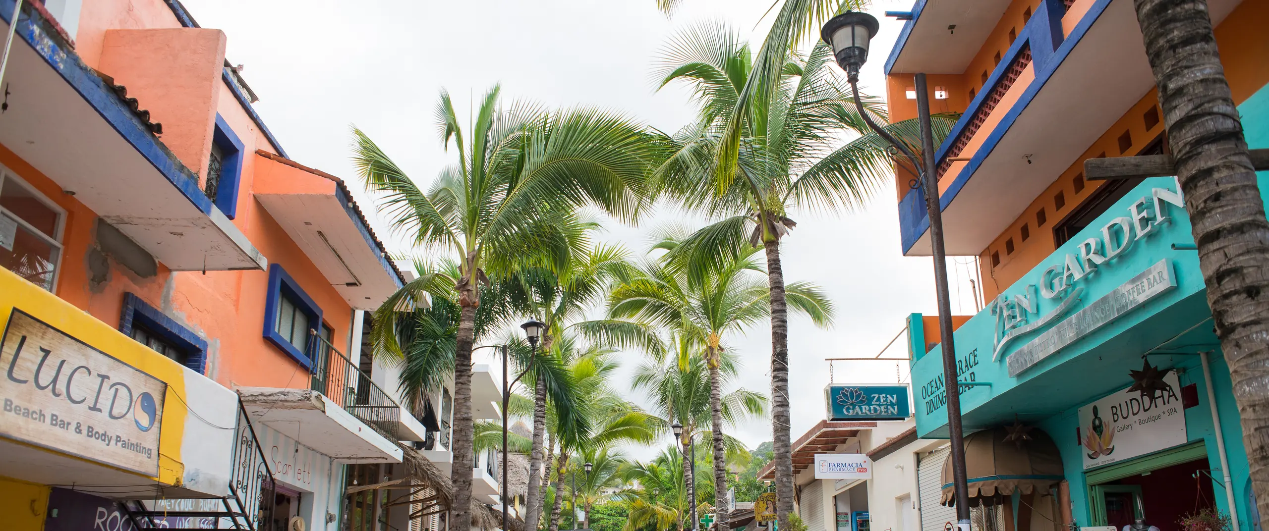 Una calle con palmas y edificios de dos pisos de colores en Sayulita, costa arriba de Punta Mita.